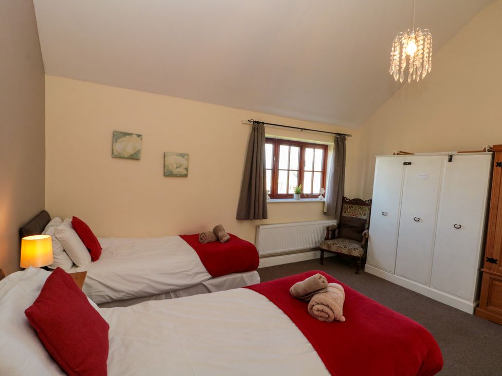 A bedroom with two beds with red blankets and pillows a window a chair and a white wardrobe at Partridge Cottage neaer Filey