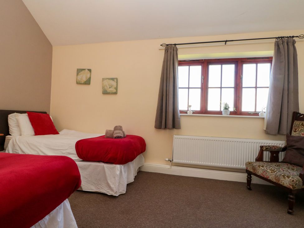 A bedroom with two single beds with red blankets a window with curtains and a patterned armchair at Partridge Cottage neaer Filey