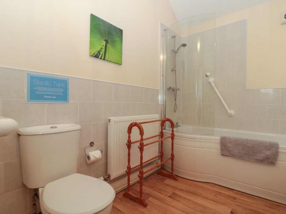 A bathroom with a toilet, bathtub with shower, towel rail, radiator, and a green leaf artwork on the wall at Partridge Cottage neaar Filey