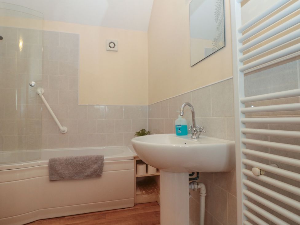 A bathroom with a bathtub a sink a mirror a towel rack and a bottle of hand soap at Partridge Cottage neaer Filey