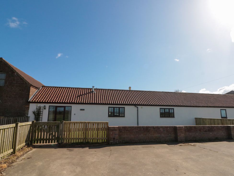 A single story white building with brown tiled roof and wooden fence under blue sky at Partridge Cottage neaer Filey
