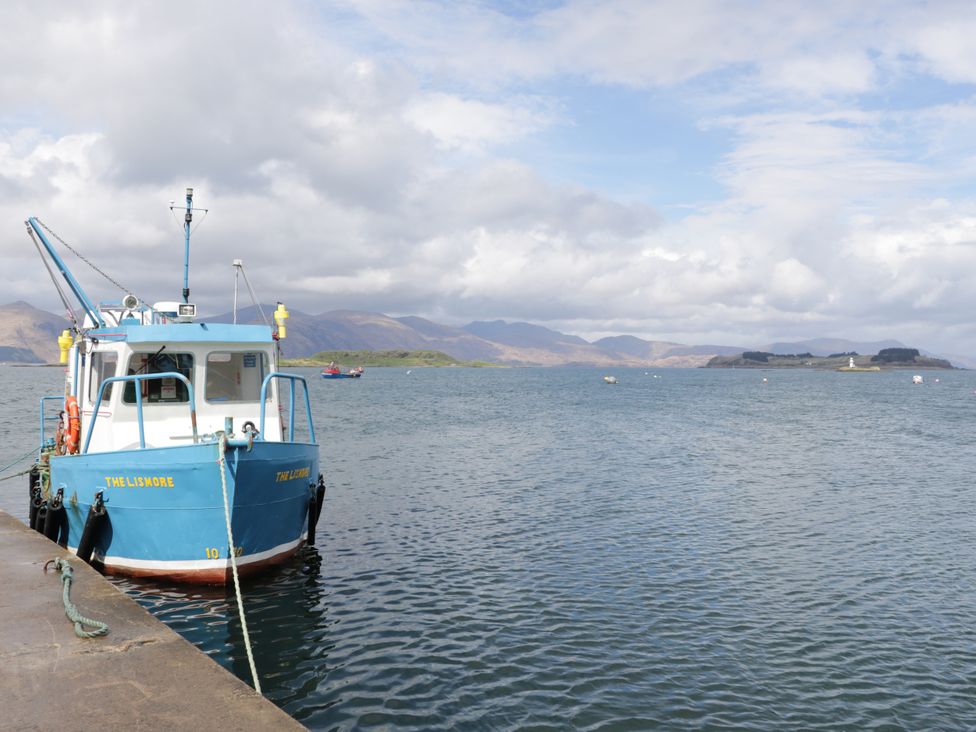 A boat at the pier with water and mountains at Tirlaggan Úr Lismore
