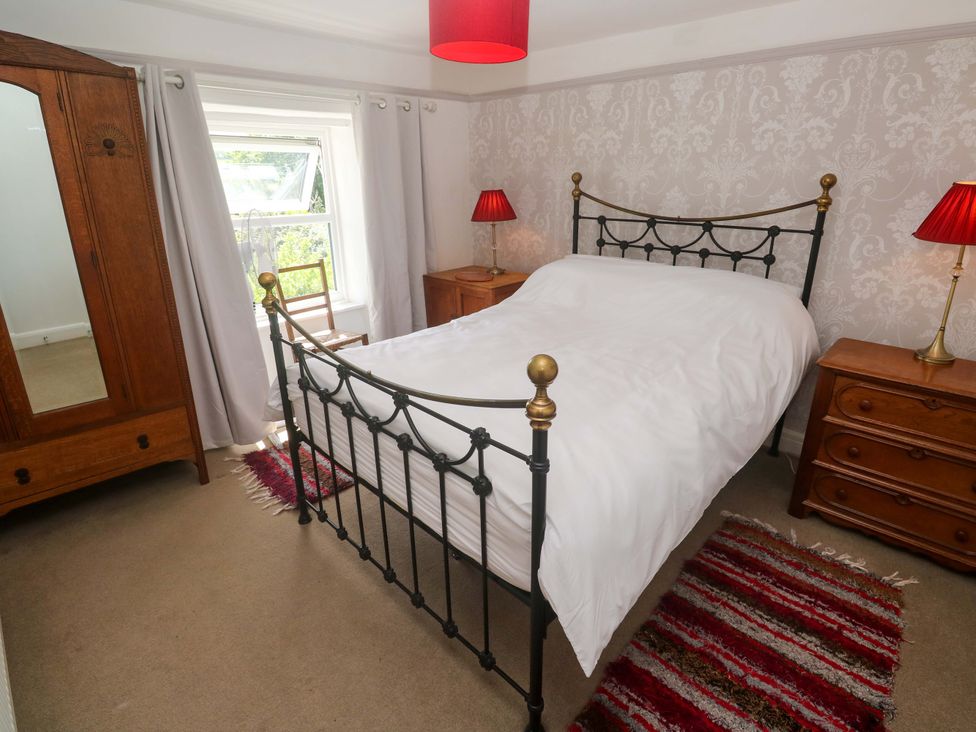 A bedroom with a bed, wardrobe, chair, lamps, and rug at Greenways in Perranporth