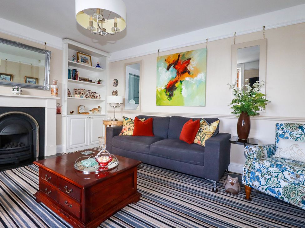 A living room with a gray sofa red cushions floral armchair a wooden coffee table fireplace and built in shelves at Cathedral View Cottage in Truro