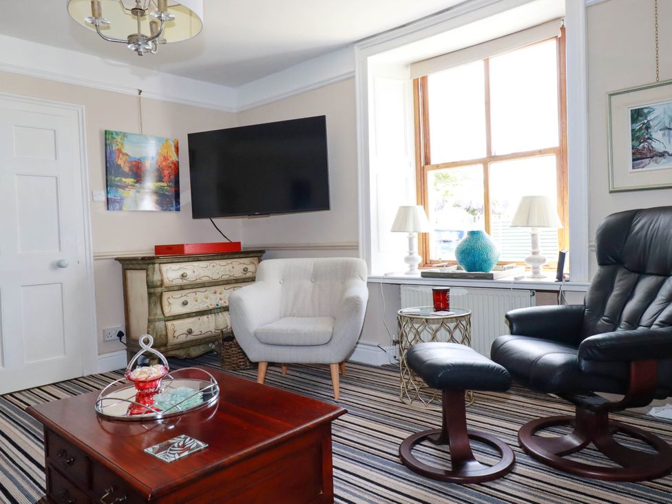 A living room with a striped carpet a wooden coffee table and white and black chairs at Cathedral View Cottage in Truro