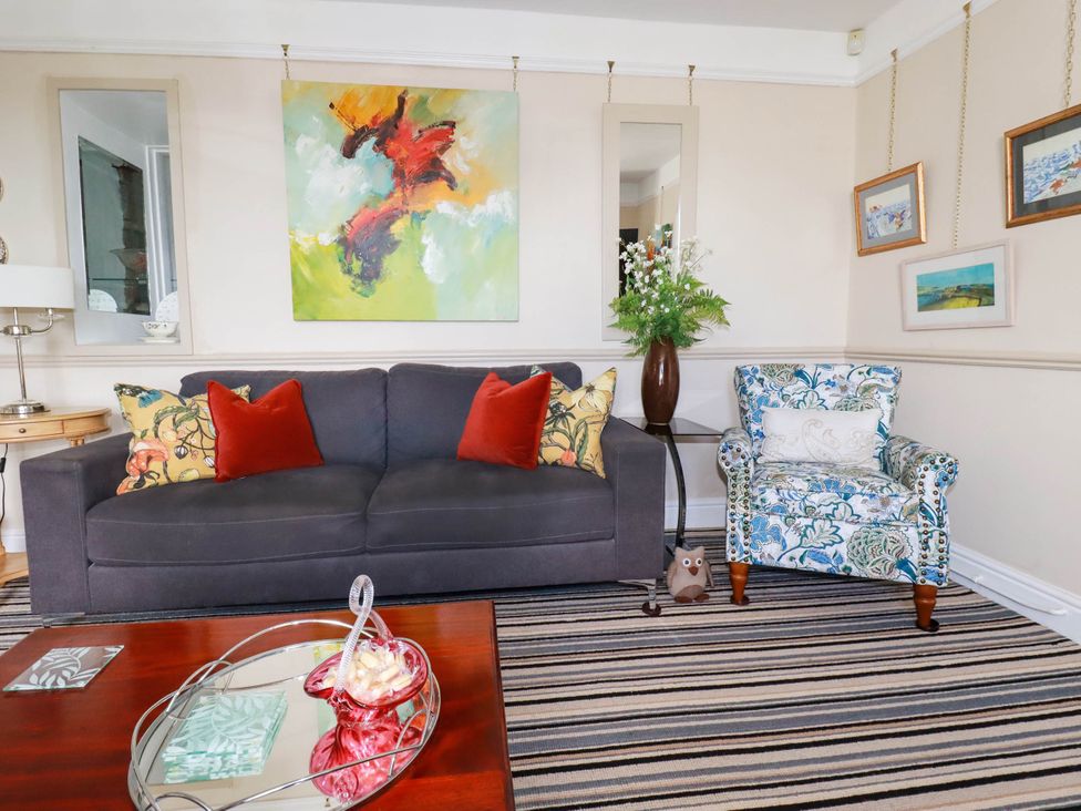 A living room with a gray sofa, floral armchair, striped carpet, and abstract painting at Cathedral View Cottage in Truro