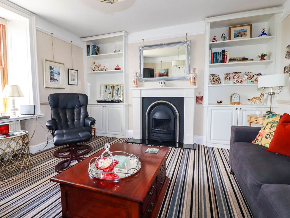 A living room with striped carpet a black armchair a grey sofa a wooden coffee table and a fireplace at Cathedral View Cottage in Truro