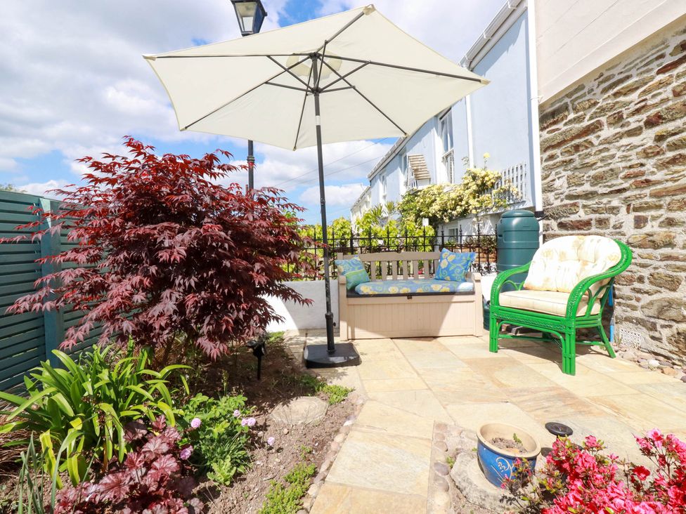 An outdoor patio with a white umbrella a bench with cushions a green chair and various plants at Cathedral View Cottage in Truro