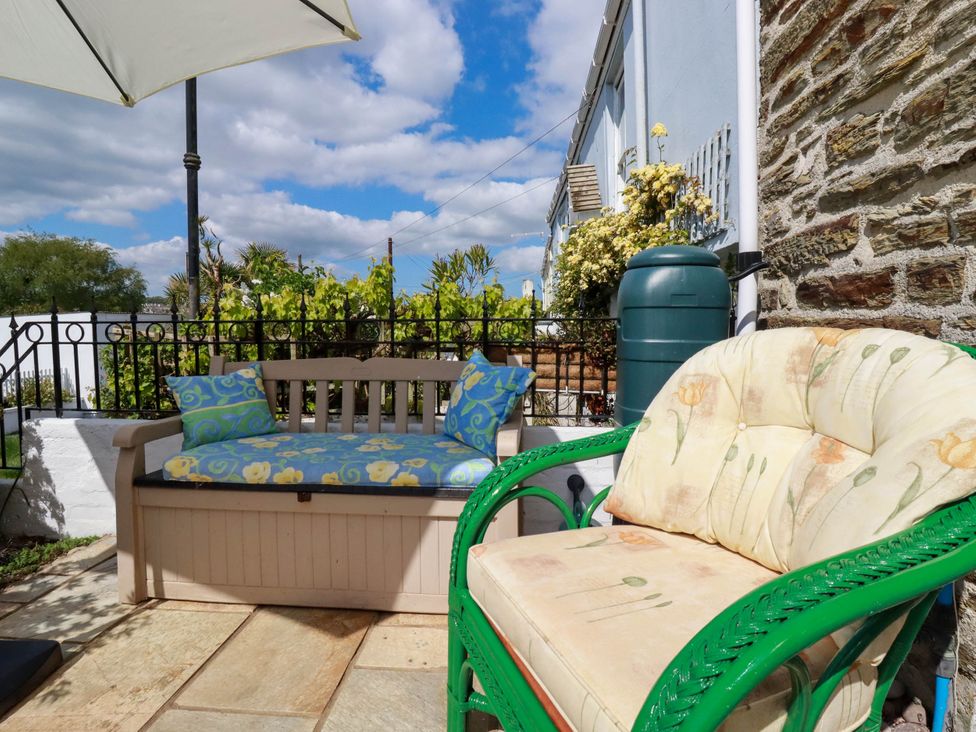 Outdoor seating area with a cushioned bench and armchair under an umbrella at Cathedral View Cottage in Truro