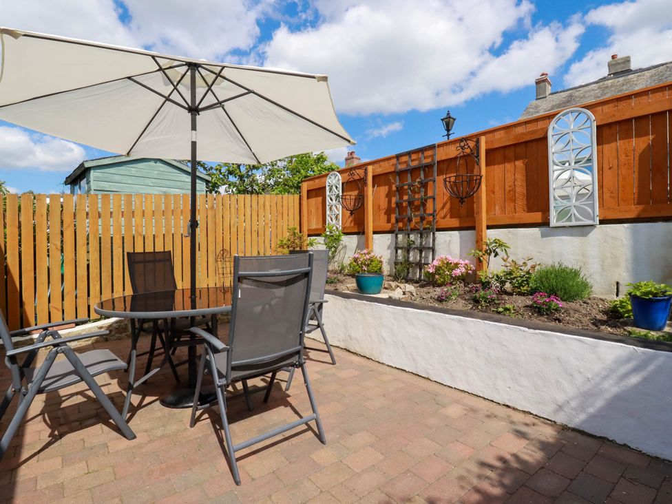 An outdoor patio with a round glass table chairs and a large white umbrella next to a flower bed and wooden fence at Cathedral View Cottage in Truro