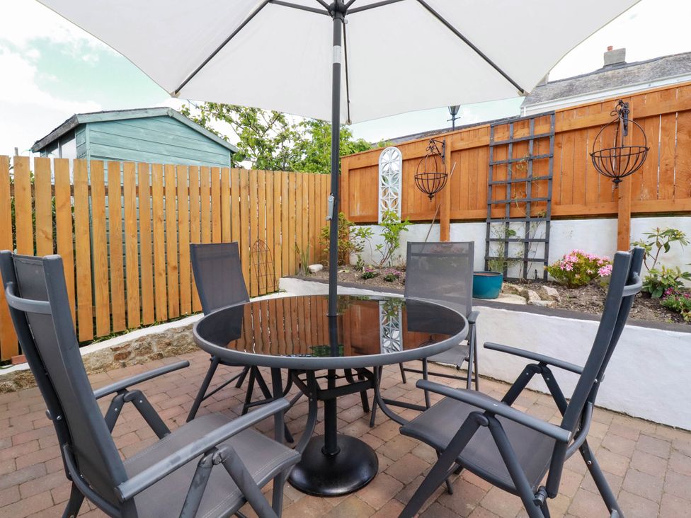 An outdoor patio with a round glass table and four chairs under a large umbrella at Cathedral View Cottage in Truro