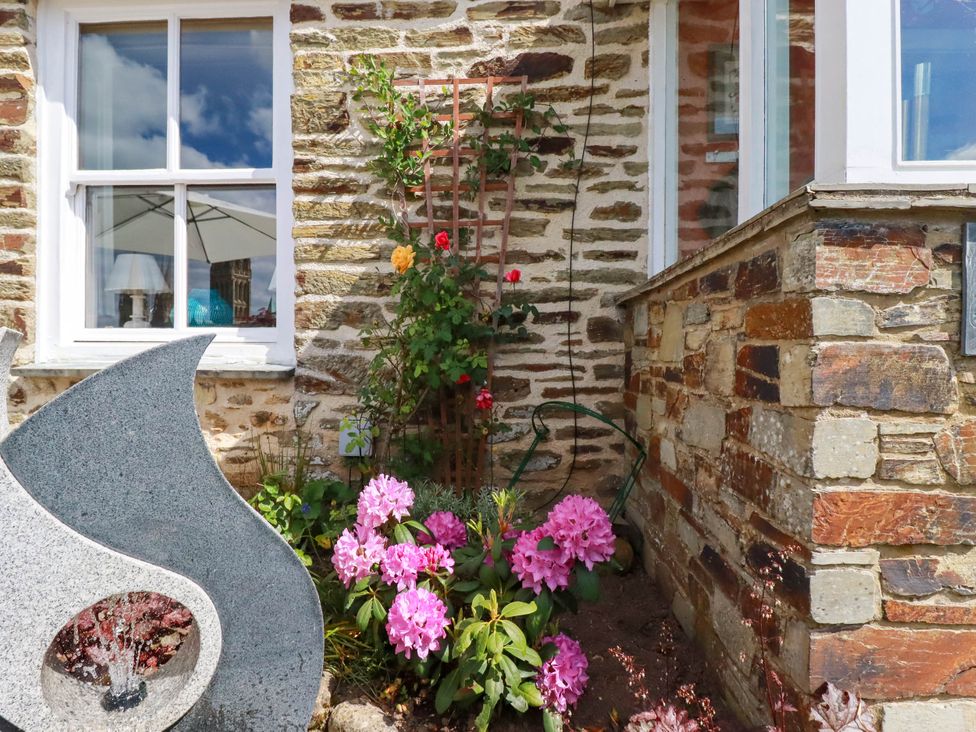A stone garden wall with pink flowers a wooden trellis with climbing plants and a stone water feature at Cathedral View Cottage in Truro