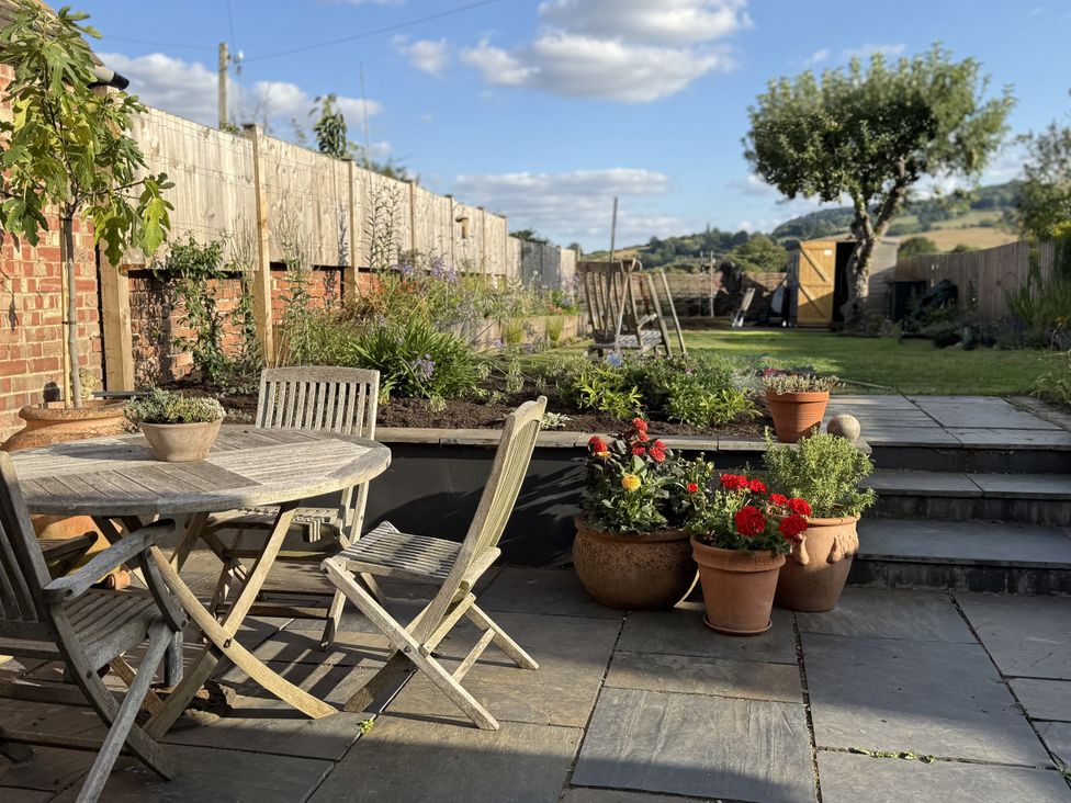 A garden with a table, chairs and flower pots at The Garden Retreat in Winchcombe