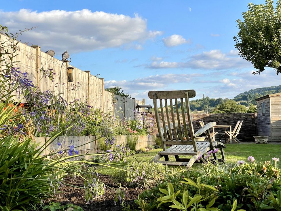 A garden with a wooden chair and table at The Garden Retreat in Winchcombe