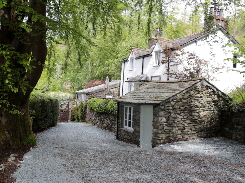 A stone building and house along a gravel driveway at Brockstone in Grasmere