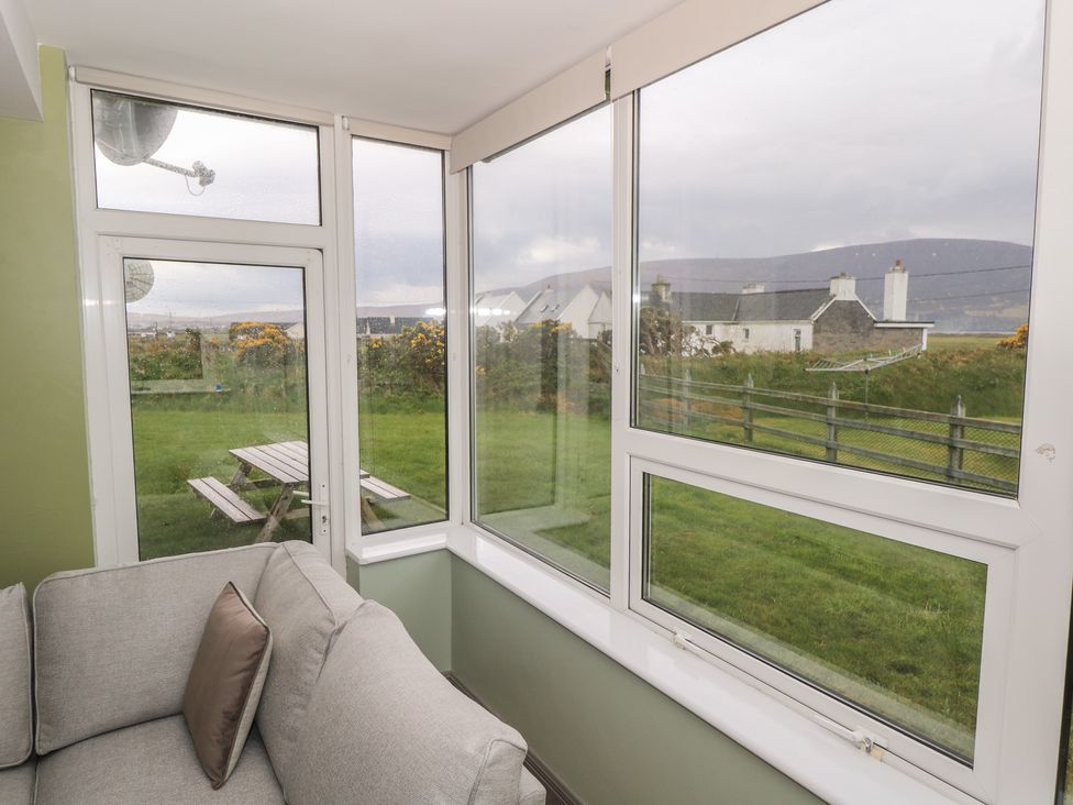A sunroom with a couch and windows overlooking grass and a picnic table at No.3 Beach Cottages Keel, County Mayo