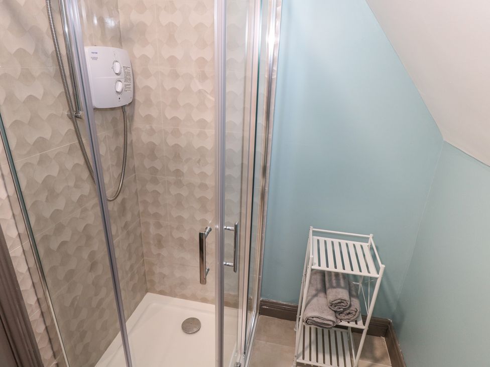 A bathroom with a shower and towels on a shelf at No.3 Beach Cottages in Keel, County Mayo