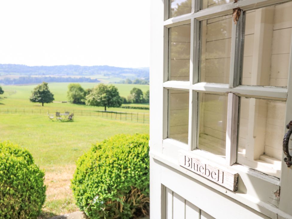 A white door with panes of glass opens to a green field with trees and outdoor furniture at Blue Bell in Colerne