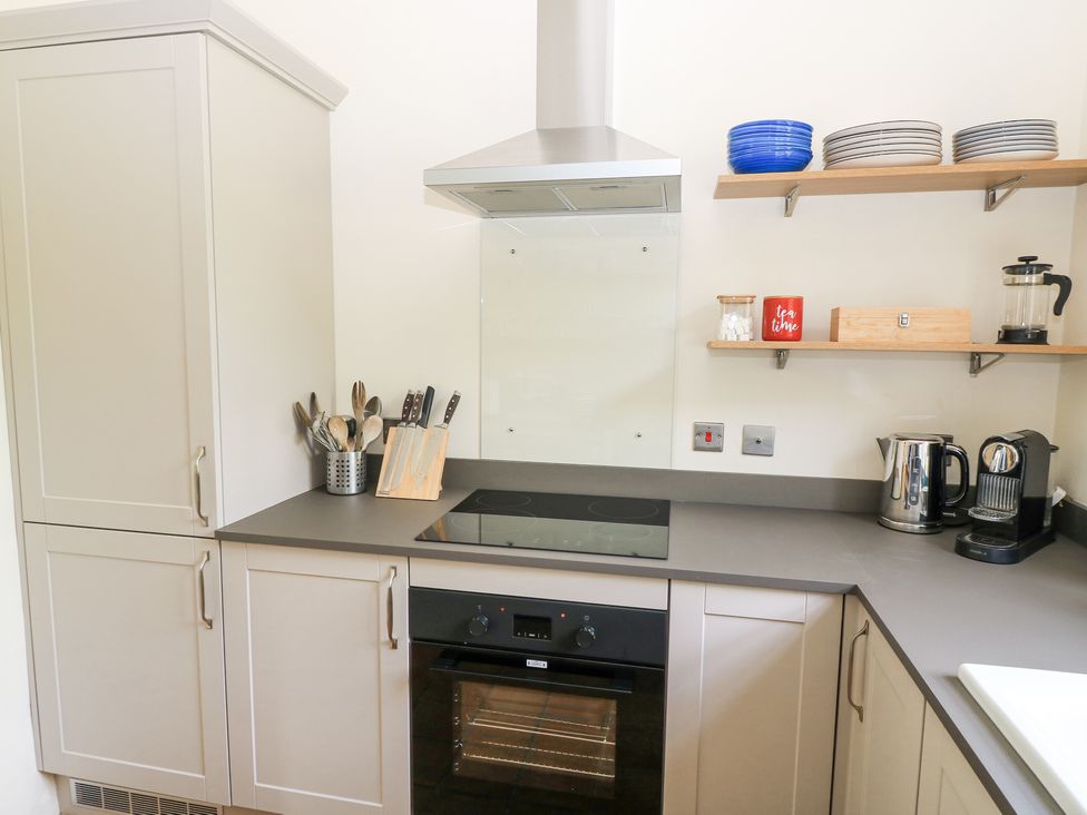 A kitchen with cabinets a stovetop an oven utensils on the counter and shelves with plates and kitchen items at Peartree in Colerne