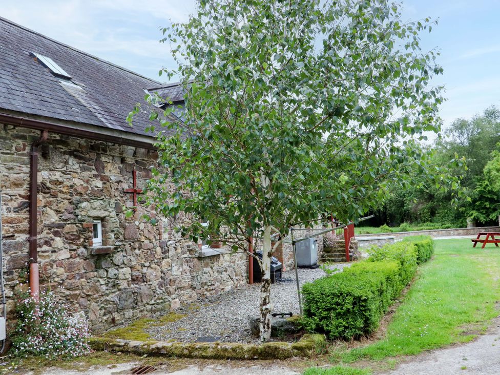 An outdoor view of a stone building with a tree and gravel path at Orchard Barn in Wexford