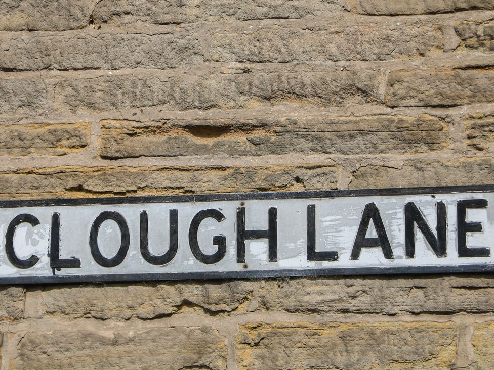 A sign that reads Clough Lane against a stone wall at Brook Cottage in Hayfield, High Peak