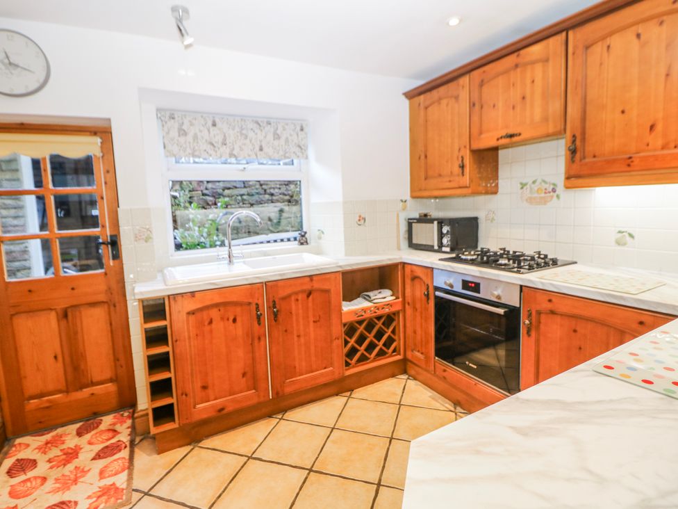 A kitchen with appliances and wooden cabinets at Brook Cottage in Hayfield, High Peak