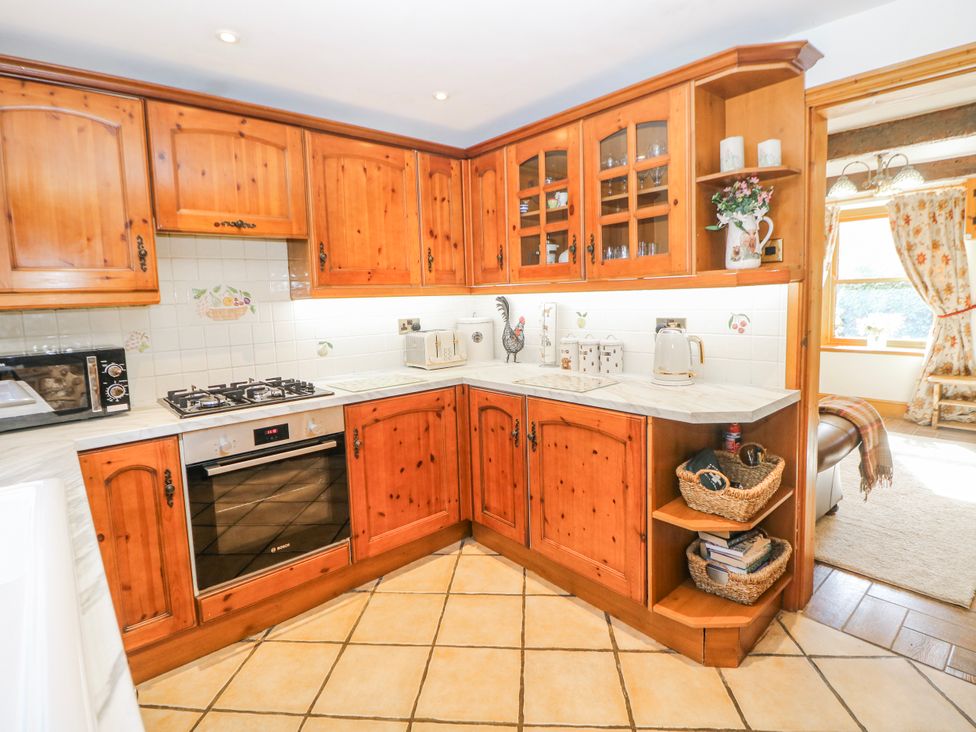A kitchen with wooden cabinets and a gas stove at Brook Cottage in Hayfield, High Peak