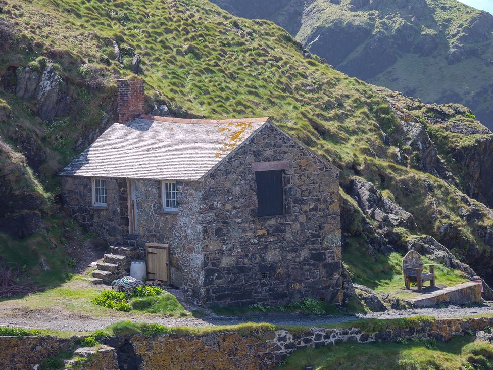 A stone cottage with steps and a chair at Morwenna in Mullion