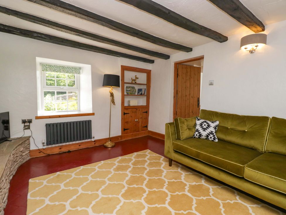 A living room with a sofa, rug, and shelves at Burnbank Cottage in Grange-Over-Sands