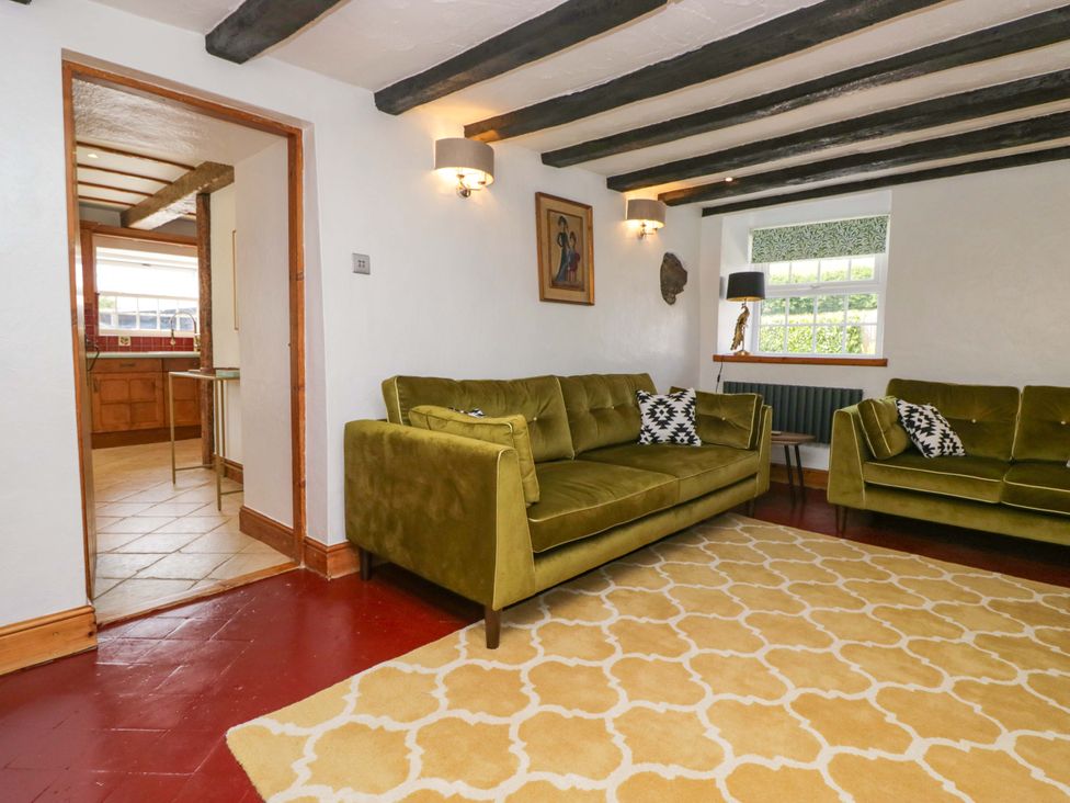 A living room with green sofas and a doorway to the kitchen at Burnbank Cottage in Grange-Over-Sands