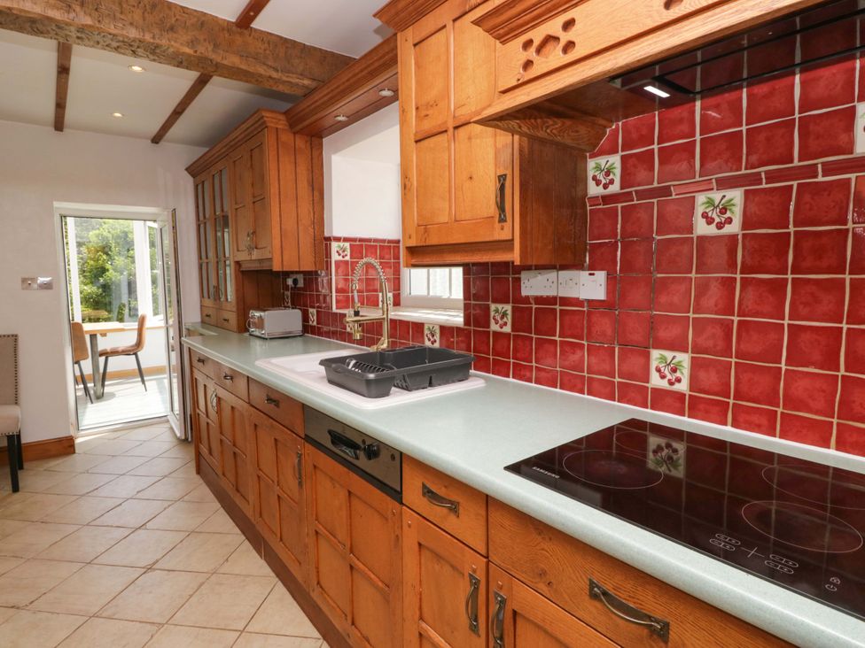 A kitchen with wooden cabinets and red tiled backsplash at Burnbank Cottage Grange-Over-Sands
