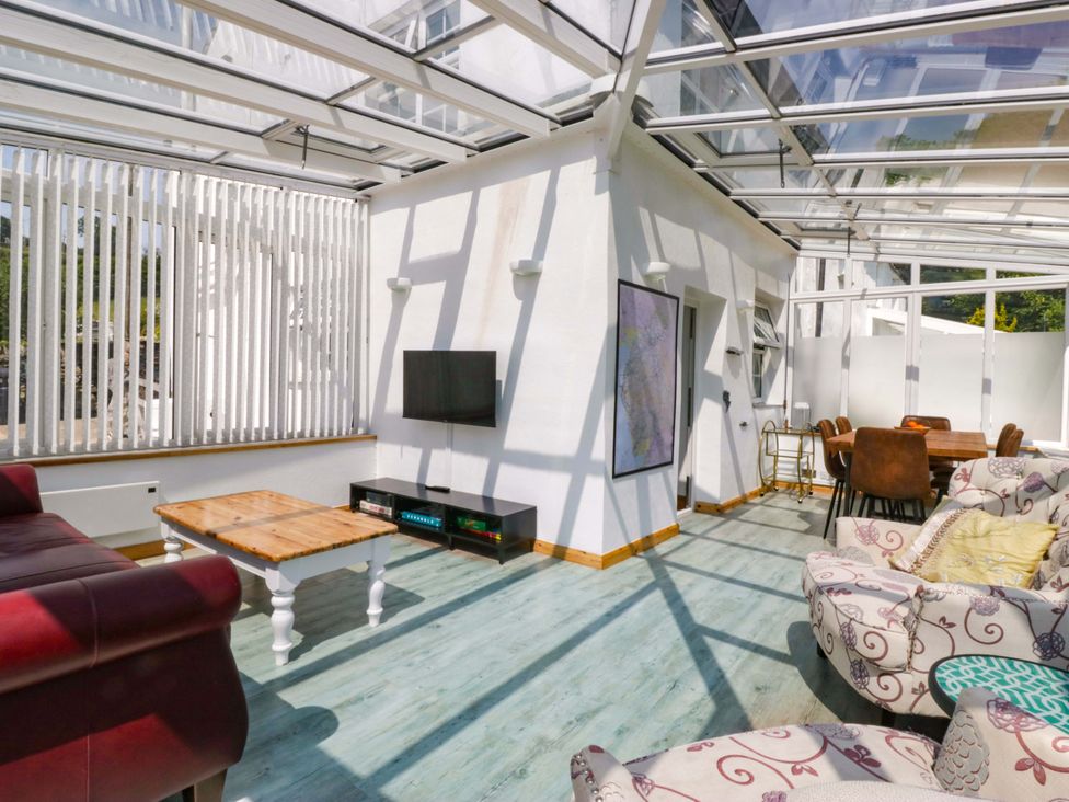 A conservatory with a coffee table and seating areas at Burnbank Cottage in Grange-Over-Sands
