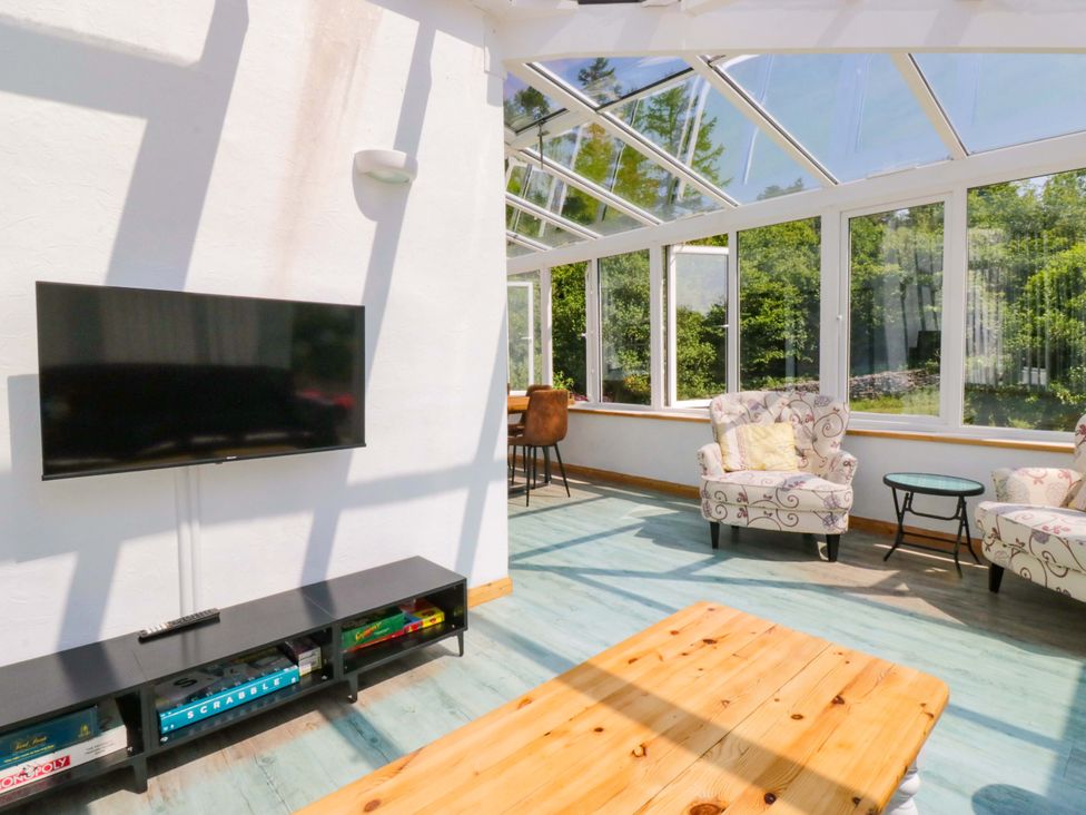 A conservatory with a TV and seating area at Burnbank Cottage in Grange-Over-Sands
