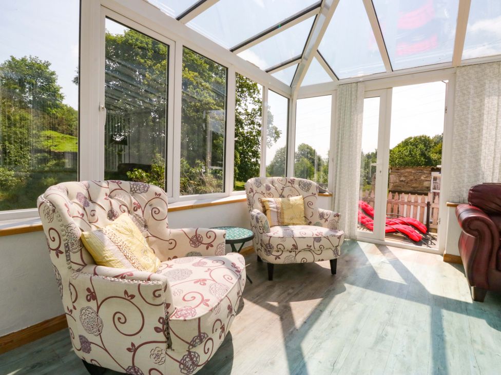 A conservatory with chairs and a table at Burnbank Cottage in Grange-Over-Sands