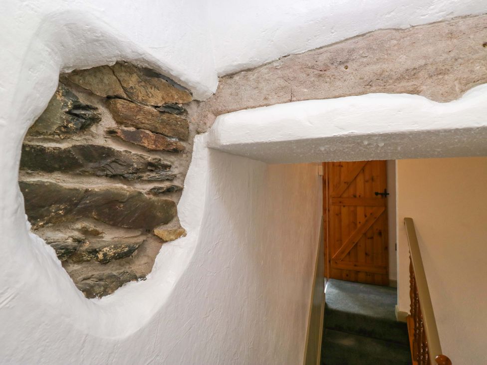 A hallway with a stone wall and wooden door at Burnbank Cottage Grange-Over-Sands