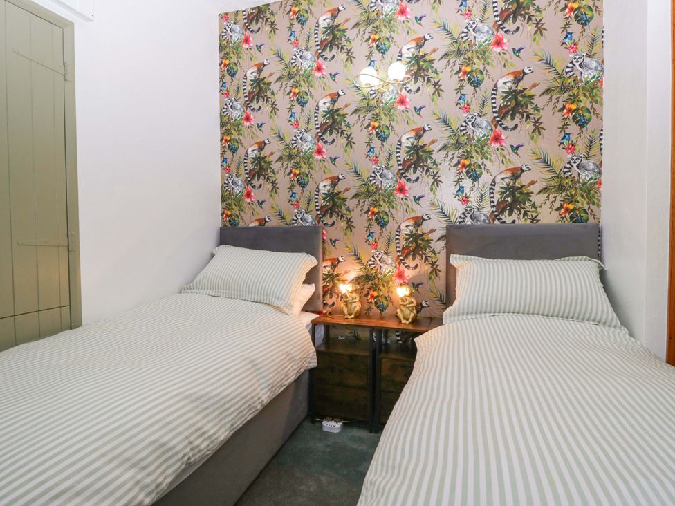 A bedroom with two beds and a bedside table at Burnbank Cottage in Grange-Over-Sands