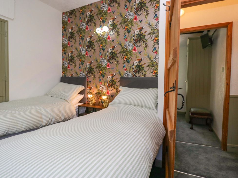 A bedroom with two beds and a door leading to another area at Burnbank Cottage Grange-Over-Sands