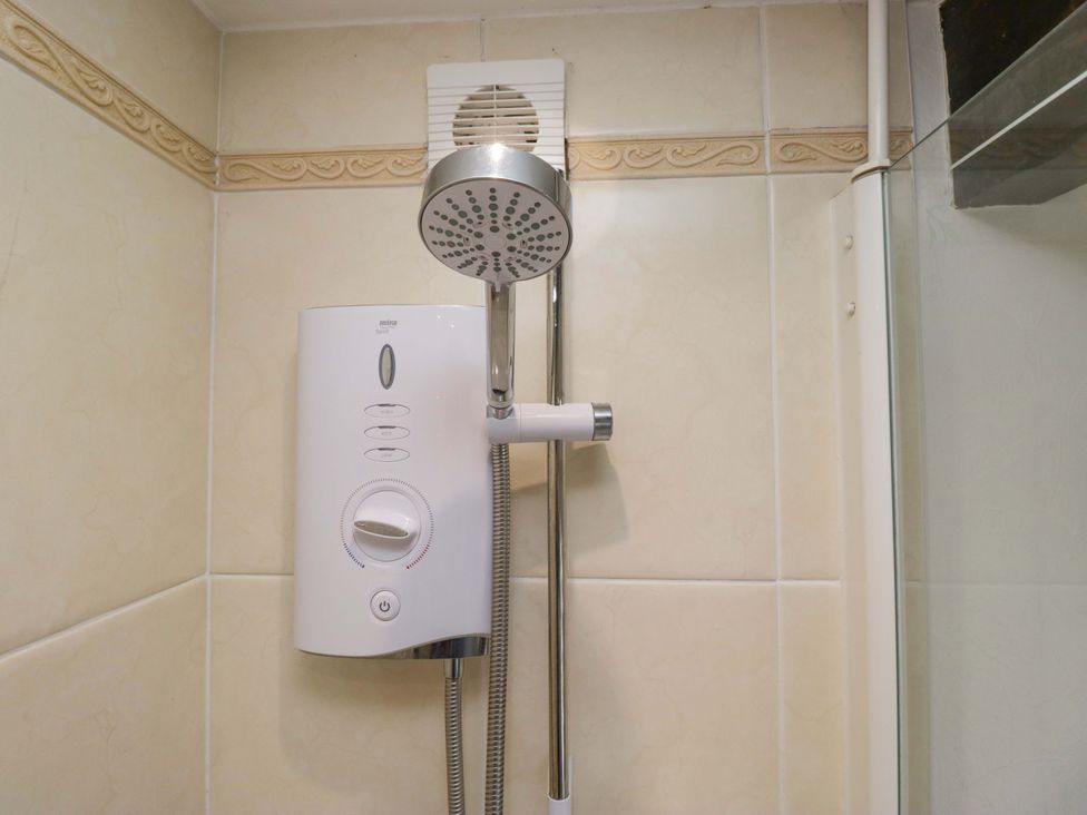 A shower unit with a shower head and control knob at Burnbank Cottage in Grange-Over-Sands