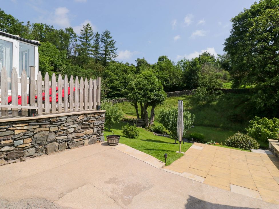 A garden with a stone wall and trees at Burnbank Cottage in Grange-Over-Sands
