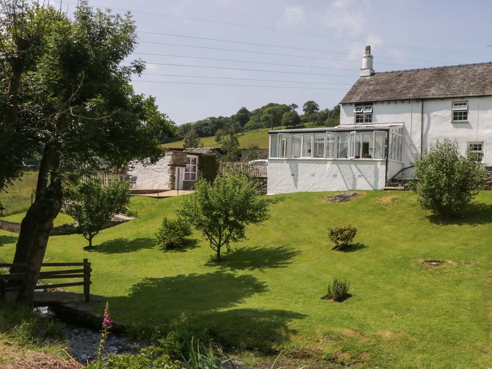A garden with a house and conservatory at Burnbank Cottage in Grange-Over-Sands