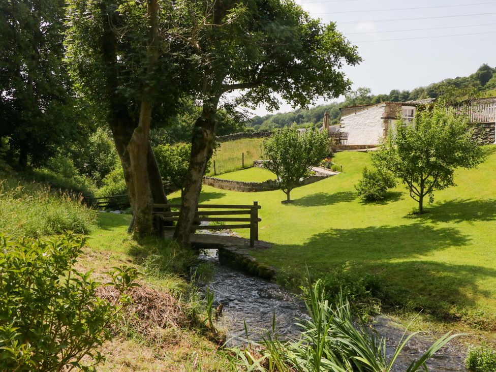 A garden with a stream, trees, and a building at Burnbank Cottage in Grange-Over-Sands