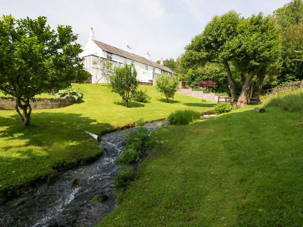 A house with a stream and trees in the garden at Burnbank Cottage Grange-Over-Sands