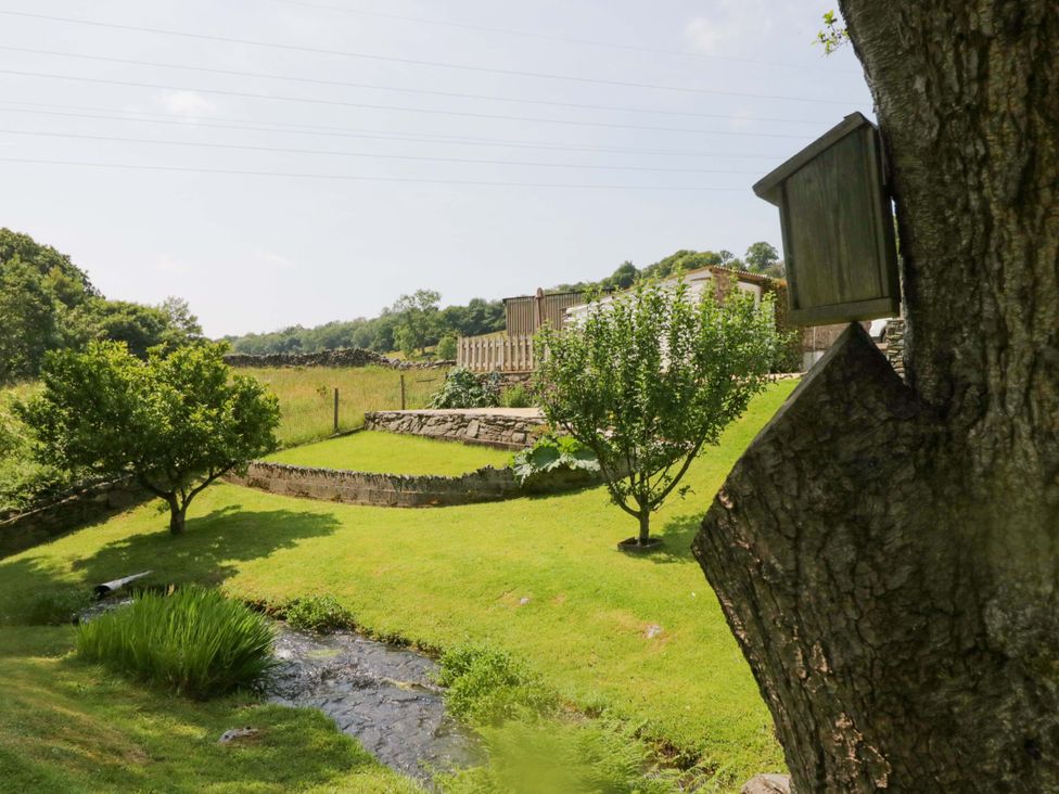 A garden with a birdhouse on a tree and a stream at Burnbank Cottage Grange-Over-Sands