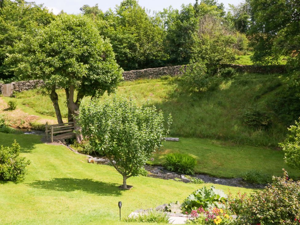A garden with a tree and a stream at Burnbank Cottage in Grange-Over-Sands