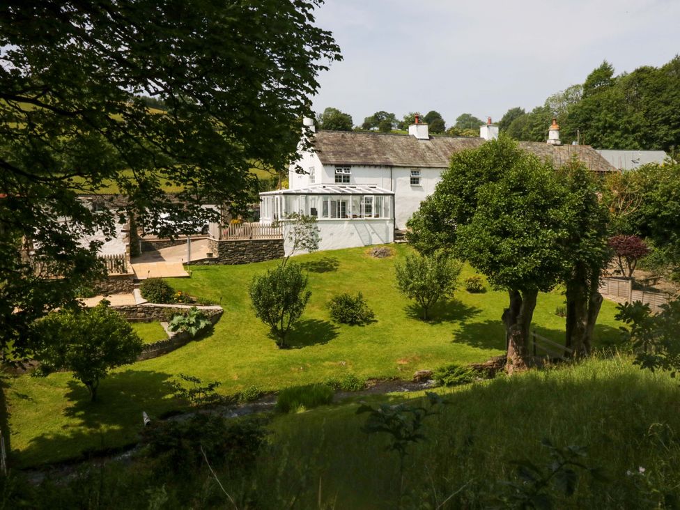 A garden with trees and a conservatory at Burnbank Cottage in Grange-Over-Sands