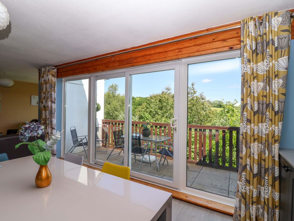 A dining area with a white table and colorful chairs next to sliding glass doors leading to a balcony with outdoor chairs and a table at 37 Tamar St Ann's Chapel near Callington