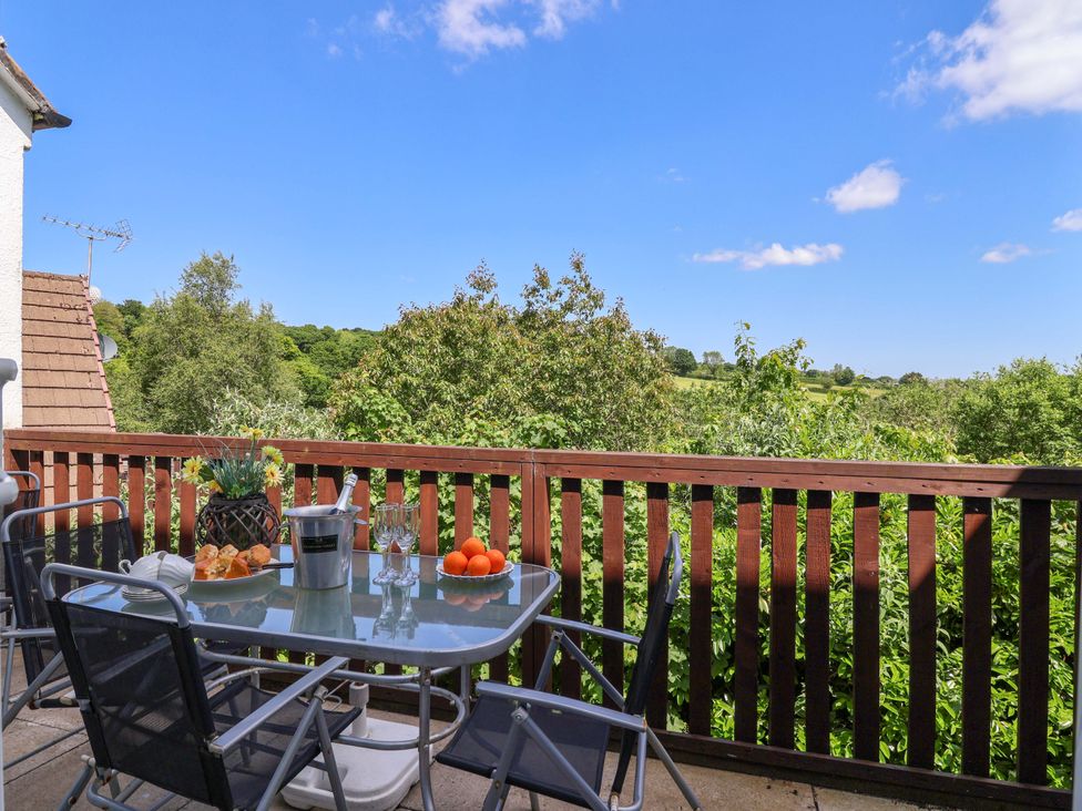 A balcony with a glass table and four chairs overlooking trees and fields at 37 Tamar St Anns Chapel near Callington