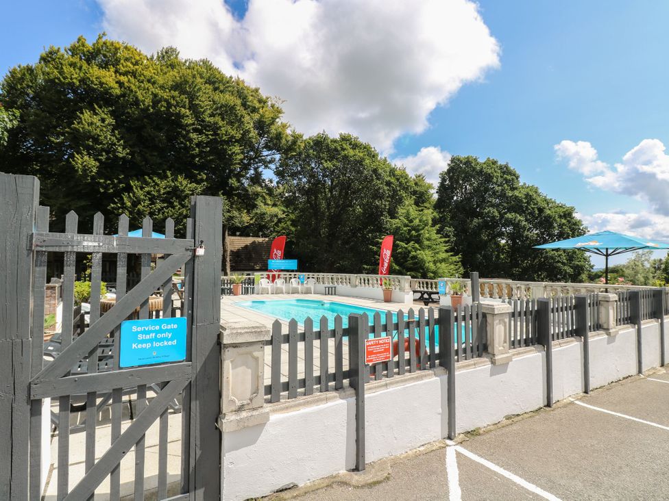An outdoor swimming pool area with fenced gate umbrellas and chairs surrounded by trees at 37 Tamar in St Ann's Chapel near Callington