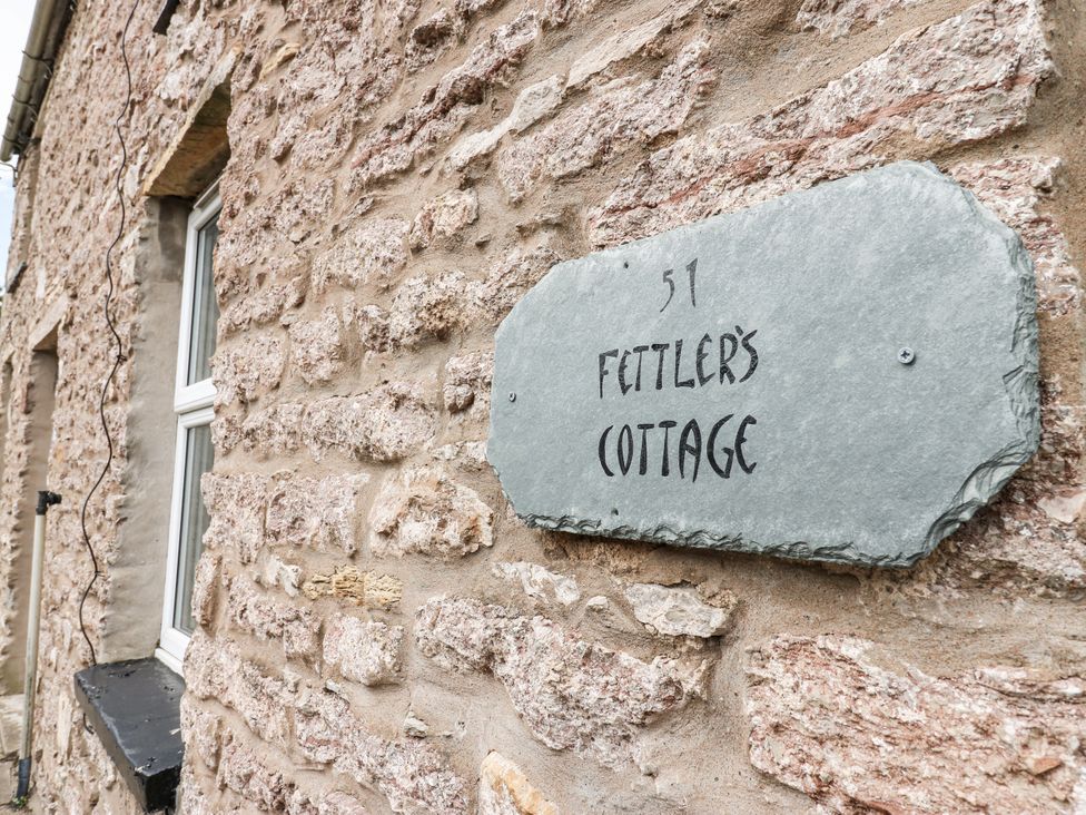 A stone wall with a slate sign displaying the name of the property at Fettlers Cottage, 51 High Street