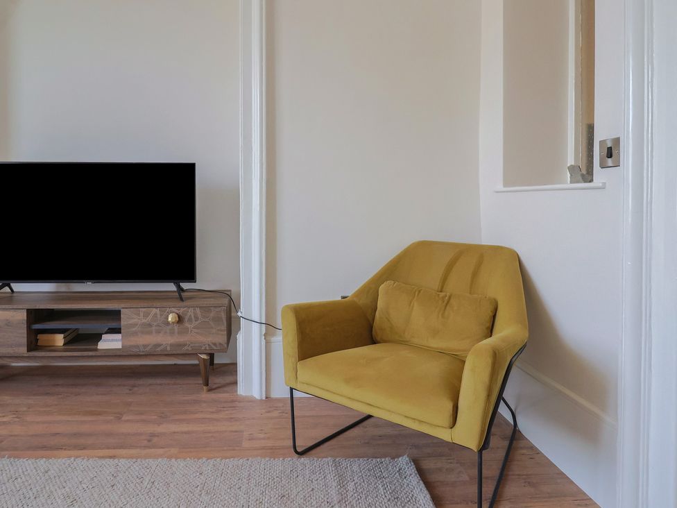 A living room with a yellow chair and television at Saltwind in Lyme Regis